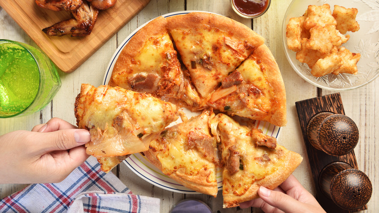 Hands lifting kimchi pizza slices