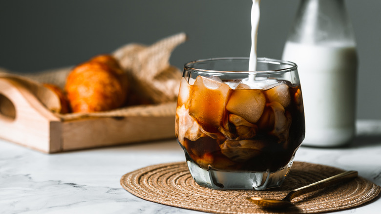 Milk being poured into a glass of iced cold brew