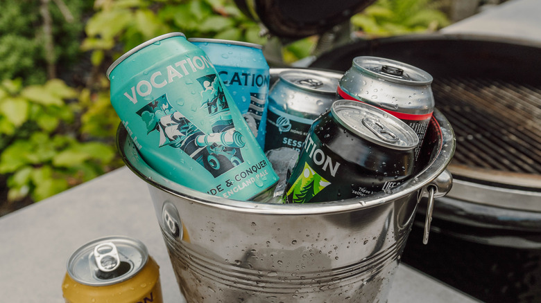 A bucket full of different Vocation beers besides a barbeque