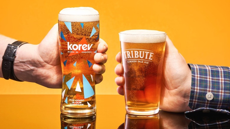 Pint of Korev and Tribute being held by two people on a table