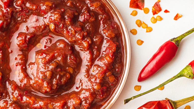 Harissa paste in bowl beside dried and fresh chili peppers