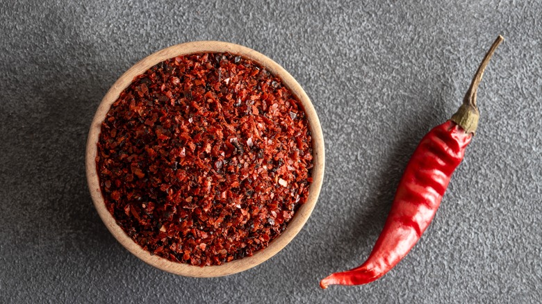 Red pepper flakes in wooden bowl beside dried red chili pepper