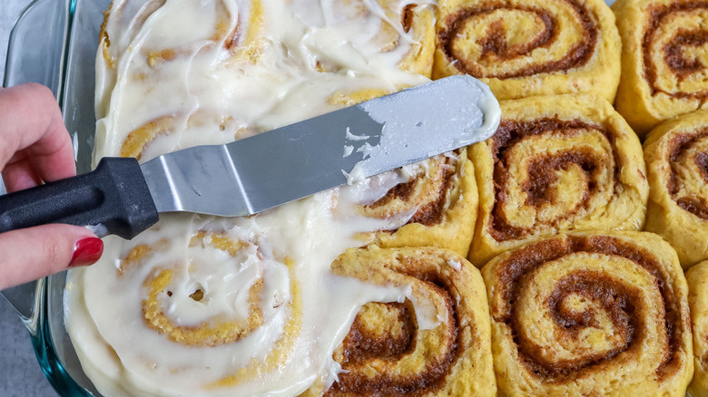 Spreading cream cheese icing onto pumpkin cinnamon rolls