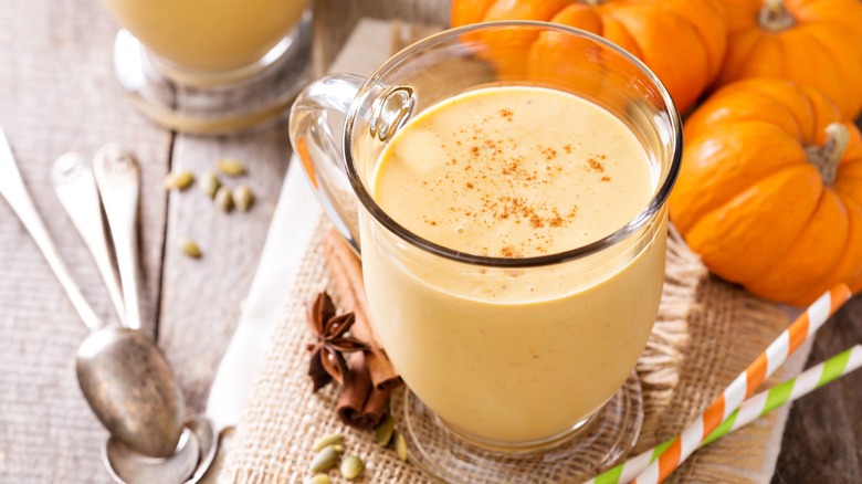 Pumpkin smoothie in glass surrounded by pumpkin gourds