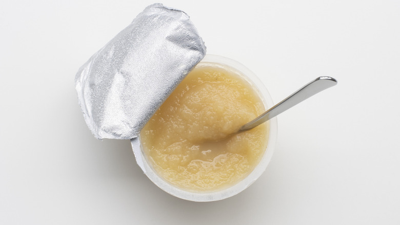 A single-serve cup of applesauce in a container has a spoon in it.