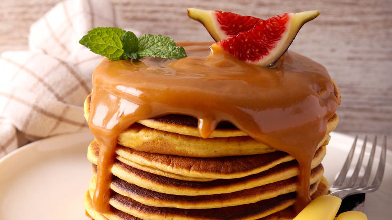 A stack of pancakes has caramel sauce dripping over it.