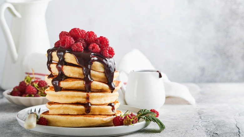 A stack of pancakes has chocolate sauce and raspberries on top.