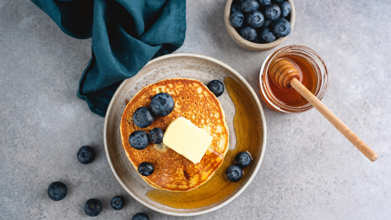 Pancakes are served with honey and some blueberries.