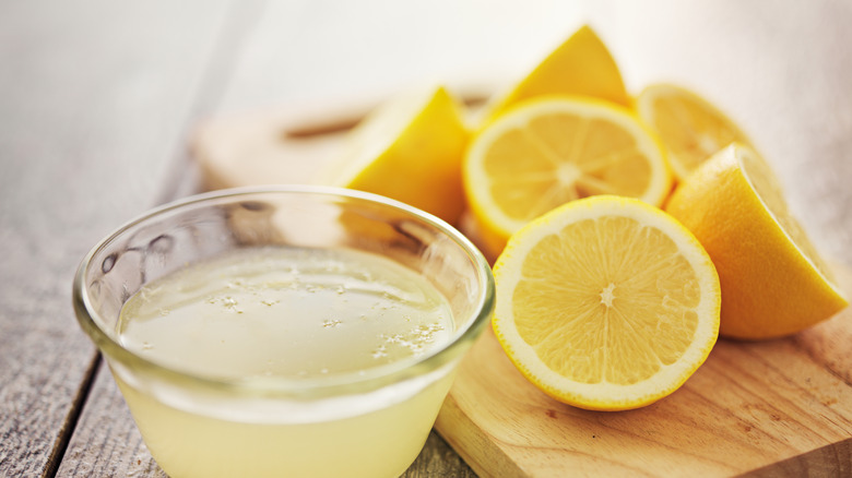 Lemon juice fills a glass cup with lemon halves behind it.