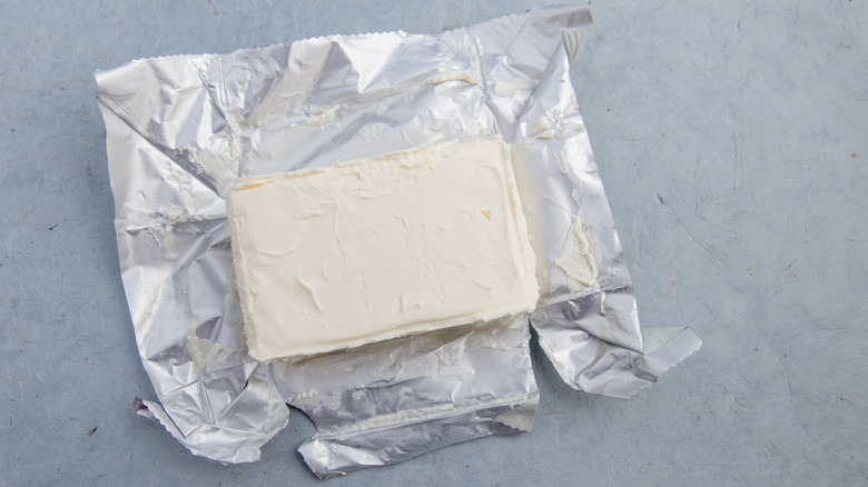 A block of cream cheese sits in the opened foil packaging.