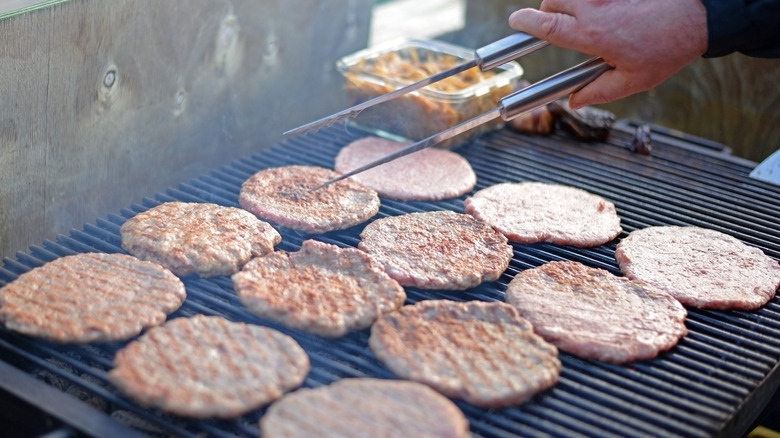 holding tongs above grilling burgers