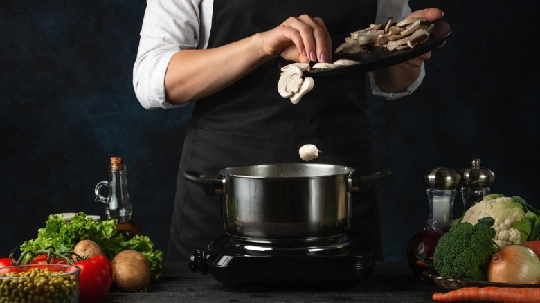 Person adding mushrooms to pot