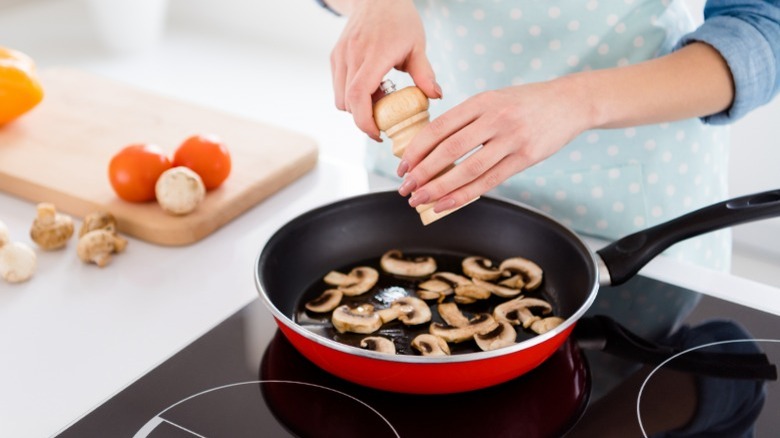 Woman salting mushrooms in pan