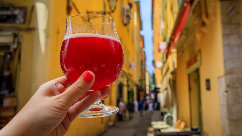 Hand holding a raspberry fruit lambic in a city street