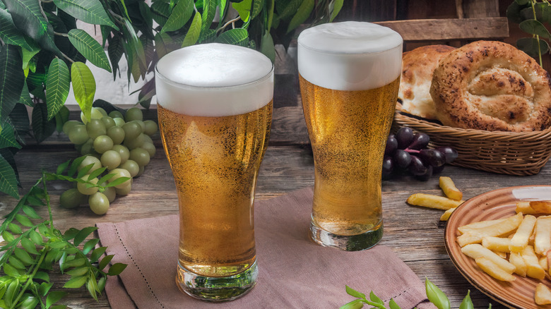 Pilsner-style glasses of beer with food and plants in background