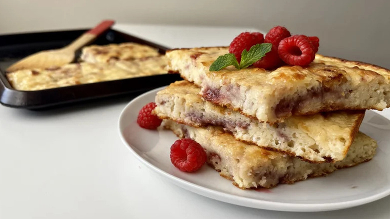 Sheet Pan Buttermilk Jammy Pancakes stacked on white plate with raspberries