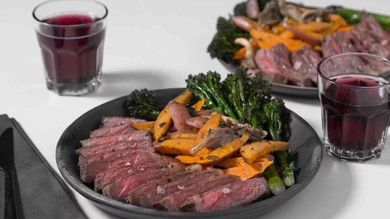 Sheet Pan Steak Dinner on black plates with cups of red wine