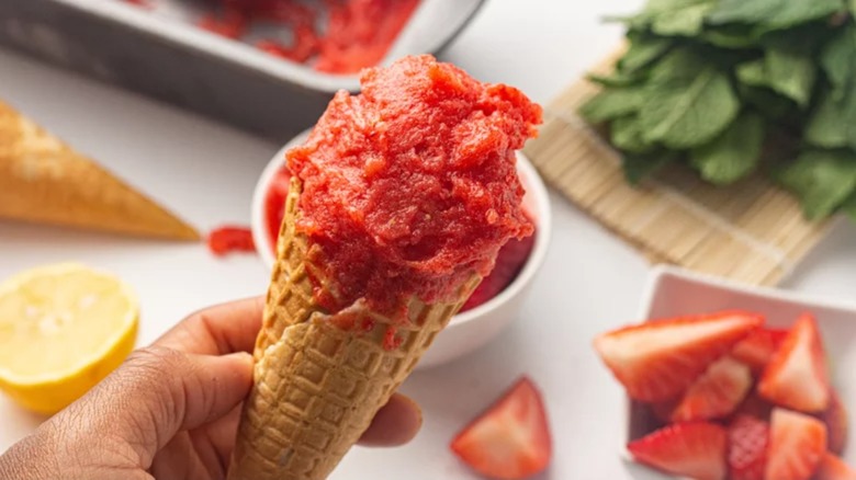 A person holding a cone with strawberry sorbet