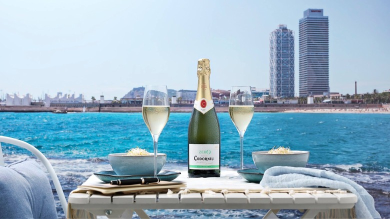 a bottle of codorniu with two wine glasses on a dining table on the waterfront