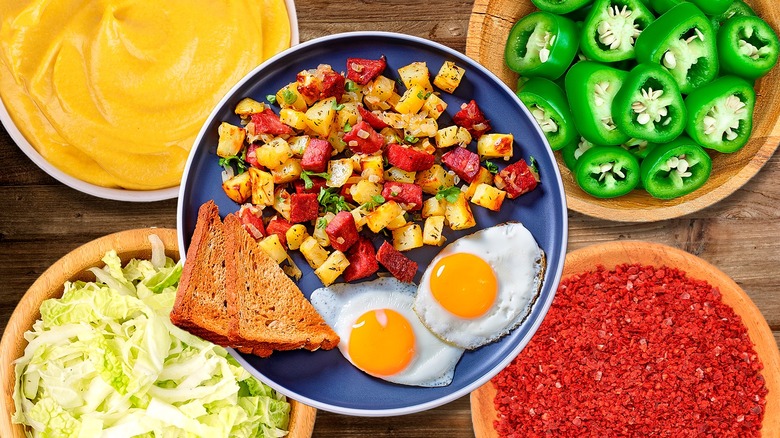 Corned beef hash and eggs in a bowl surrounded by bowls of ingredients