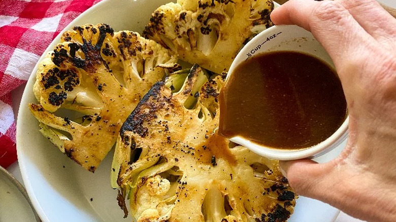 Vegan Worcestershire sauce being poured on cauliflower steaks