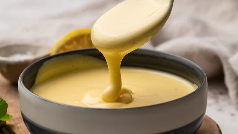 Spoonful of creamy Hollandaise sauce being taken from bowl