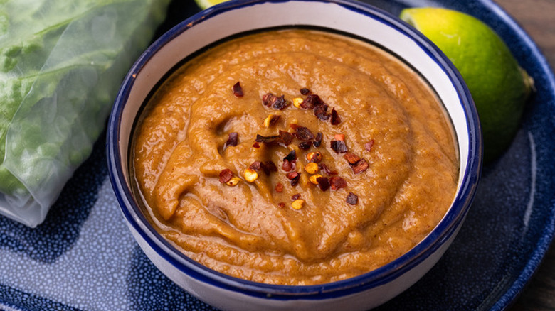 Bowl of spicy peanut sauce on serving board with limes and lettuce wrap