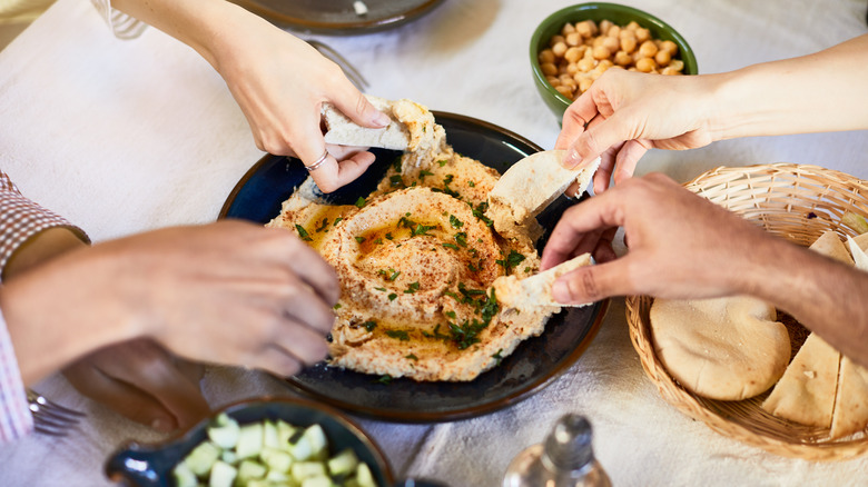 hands reaching into hummus bowl