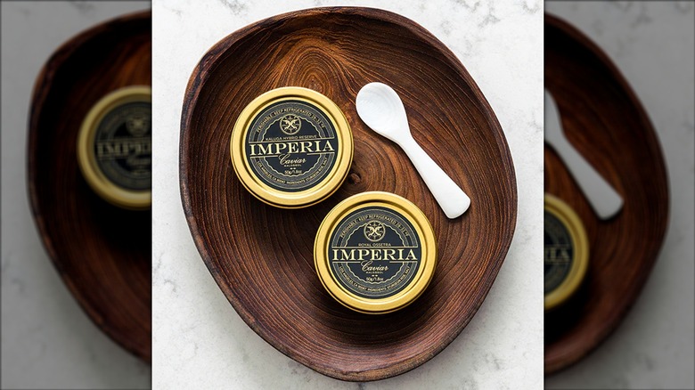 Two containers of Imperia caviar and caviar spoon in wooden dish