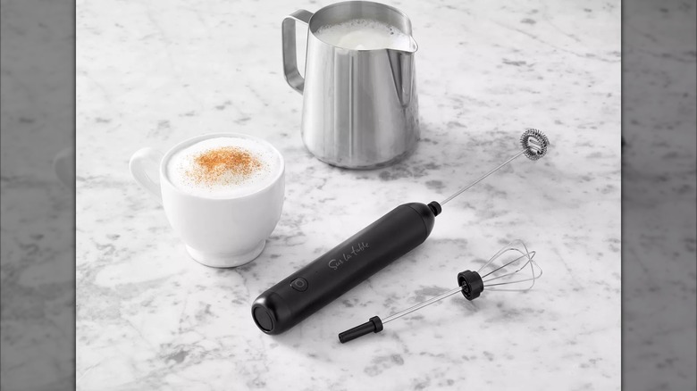 milk frother on marble countertop next to coffee cup