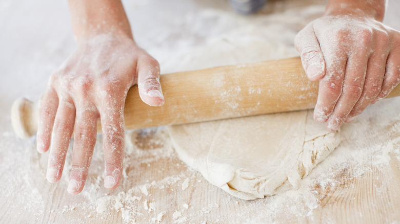 Hands rolling pie dough with flour