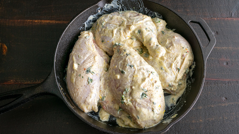 Raw chicken covered with yogurt in cast iron pan