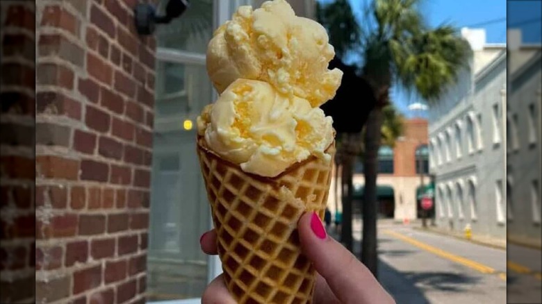 Hand holding vanilla ice cream cone in front of brick building