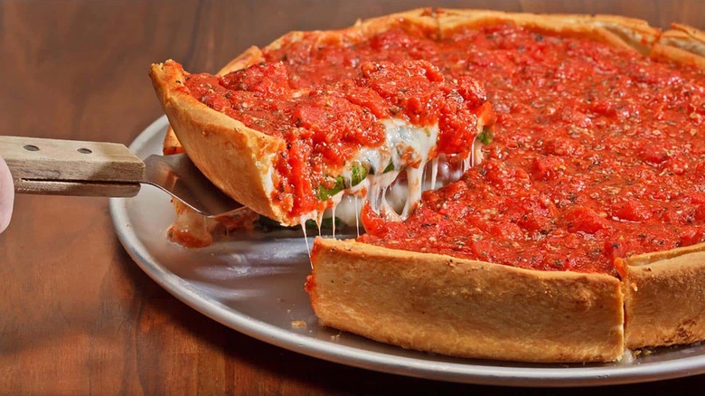 Chicago deep dish pizza with slice lifted out of it on wooden table