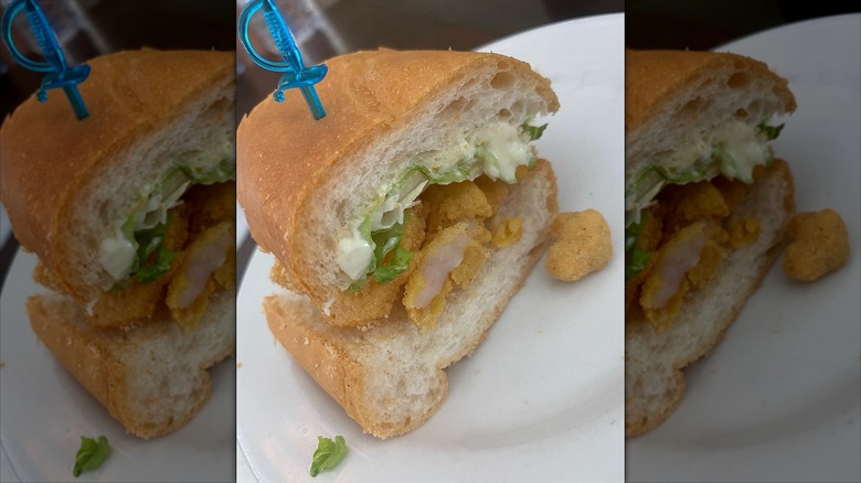 Half chicken sandwich with blue sword toothpick on white plate