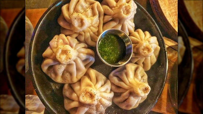 Black plate of dumplings around container of green sauce