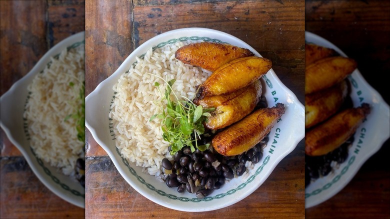 Plantains, rice, beans and microgreens in white bowl on wooden table