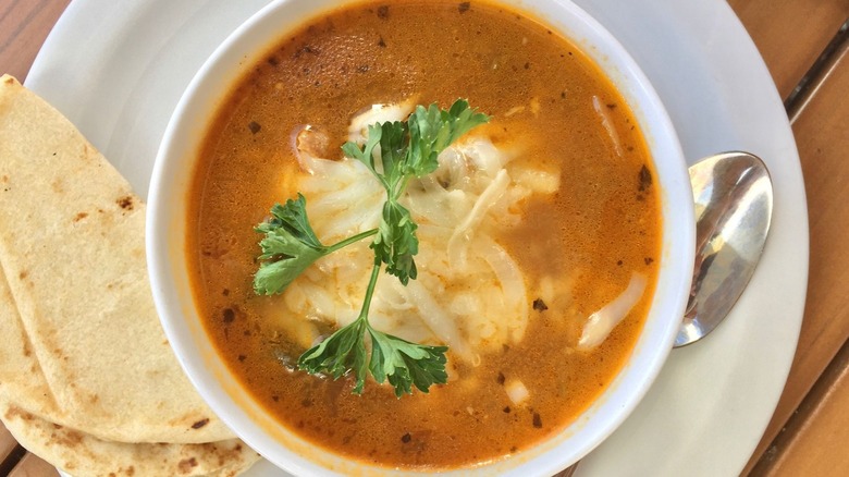 White bowl of tortilla soup next to tortilla on white plate