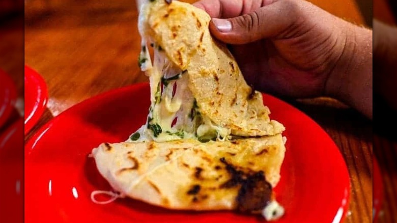 Hand pulling apart half of quesadilla on red plate