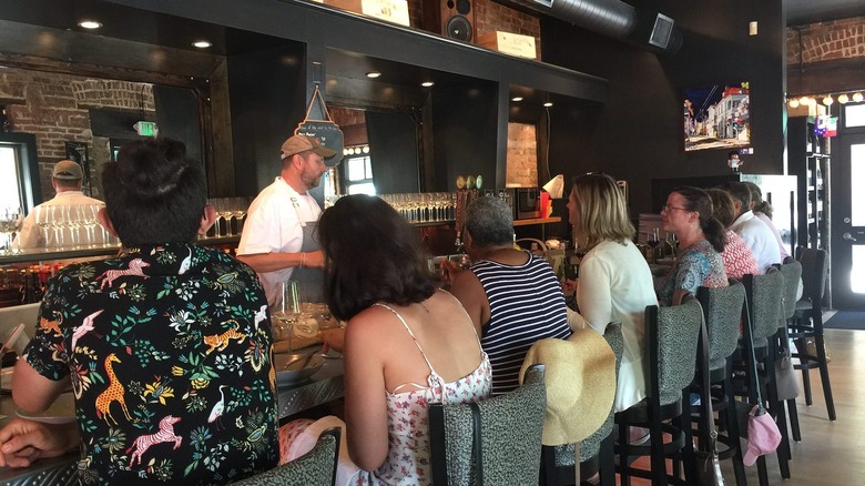 Chef behind bar teaching food class to patrons sitting at bar