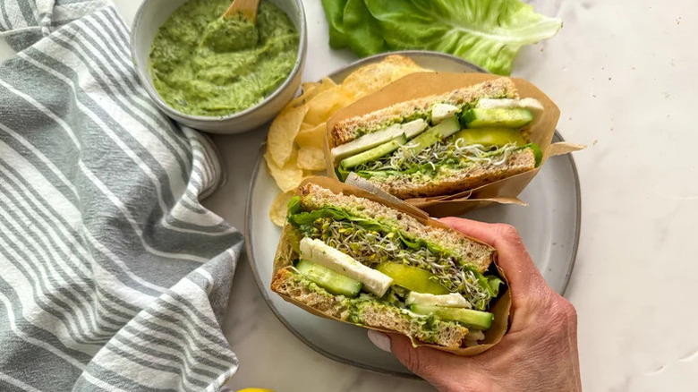 Hand holding Green Goddess Sandwich over plate