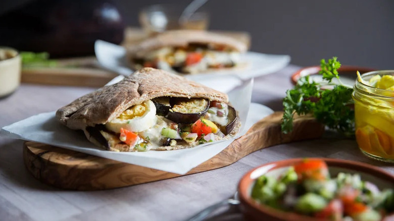 Sabich on wooden cutting board with herbs in foreground