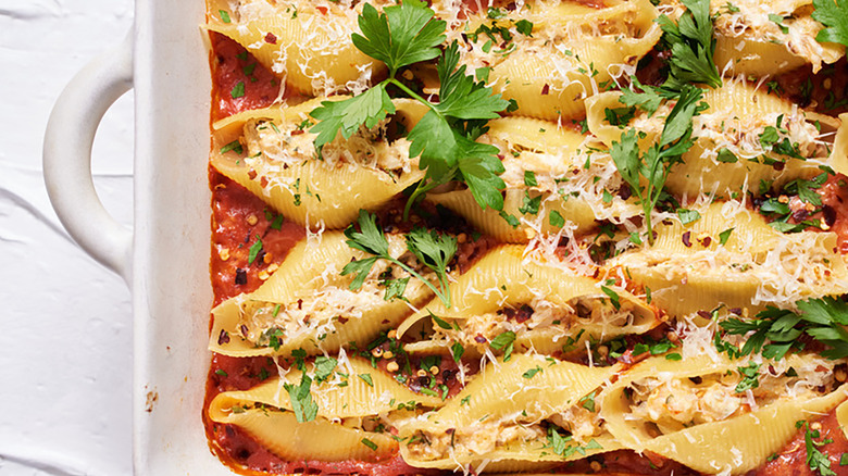 Seafood-stuffed pasta shells in baking dish with tomato sauce and parsley