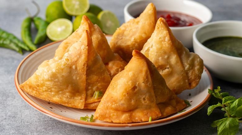 Samosas on a plate with lime, chutneys, green chilis, and mint