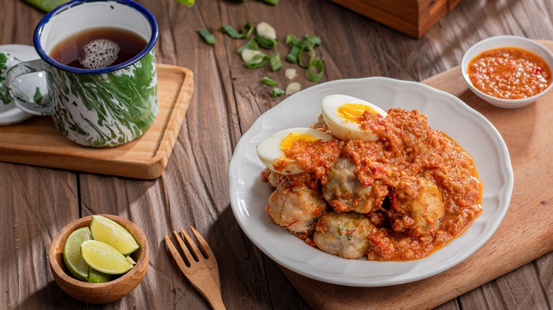 Siomay covered in peanut sauce alongside hard boiled egg, lime, and tea