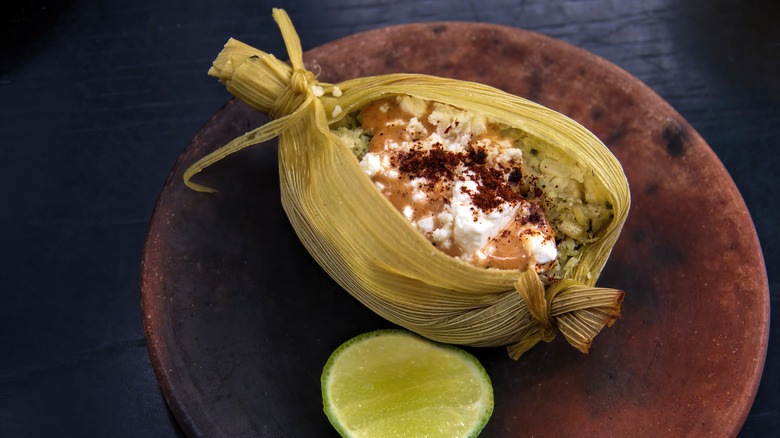 Open tamale wrapped in corn husk with slice of lime