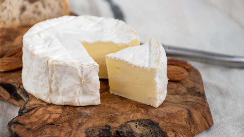 camember cheese with a wedge cut out on wooden board