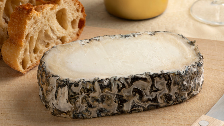 a slice of monte enebro on a board with baguette in background