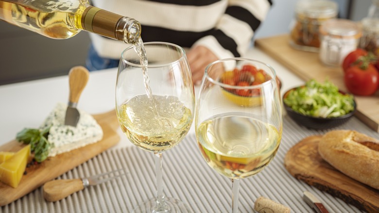 Bottle pouring two glasses of Sauvignon Blanc while preparing a charcuterie spread