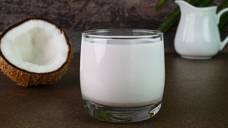 Coconut milk sits in a glass next to a halved coconut.